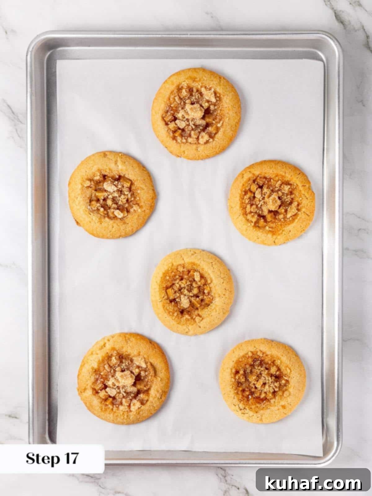 Freshly baked apple pie cookies, golden brown at the edges with bubbly apple filling and crumbly topping, cooling on a parchment-lined baking sheet straight from the oven.
