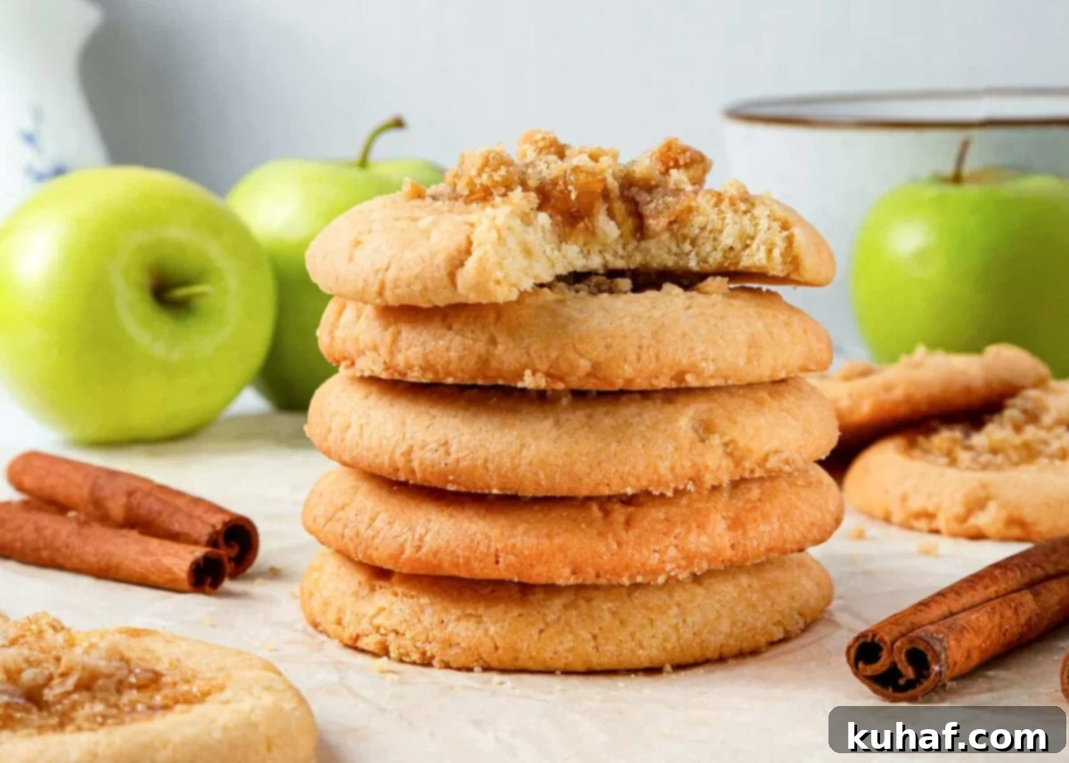Group of freshly baked apple pie cookies arranged on a cooling rack, garnished with whole green apples and cinnamon sticks for a rustic fall presentation.
