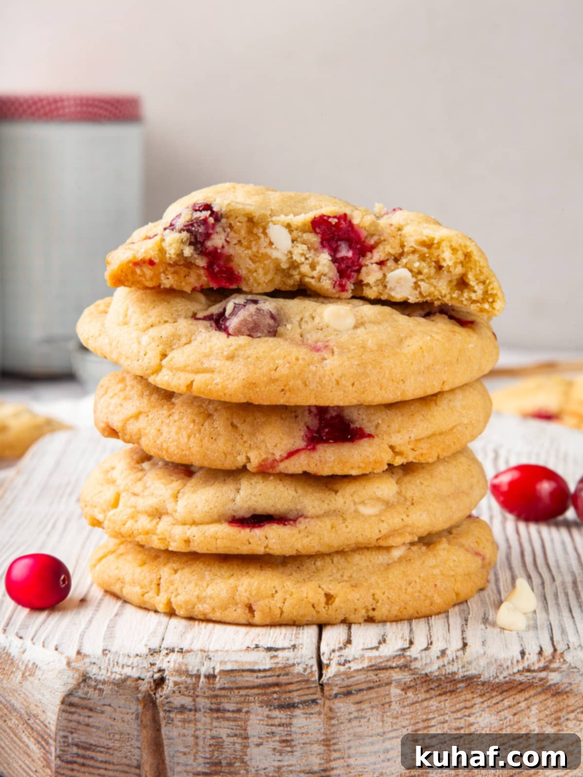 Baked cookies surrounded by scattered cranberries and crumbs on a neutral surface.