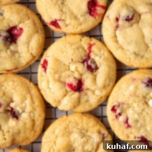 Freshly baked cookies cooling on a wire rack with cranberries and white chocolate throughout.