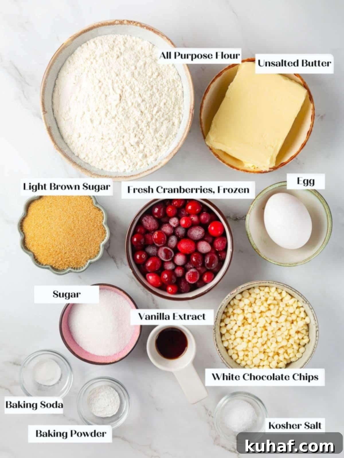 All cookie ingredients including butter, eggs, cranberries, and white chocolate laid out on a countertop.