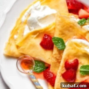 A plate of cream-filled crepes layered with fresh strawberries and golden folds.