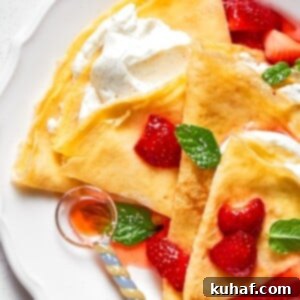 A plate of cream-filled crepes layered with fresh strawberries and golden folds.