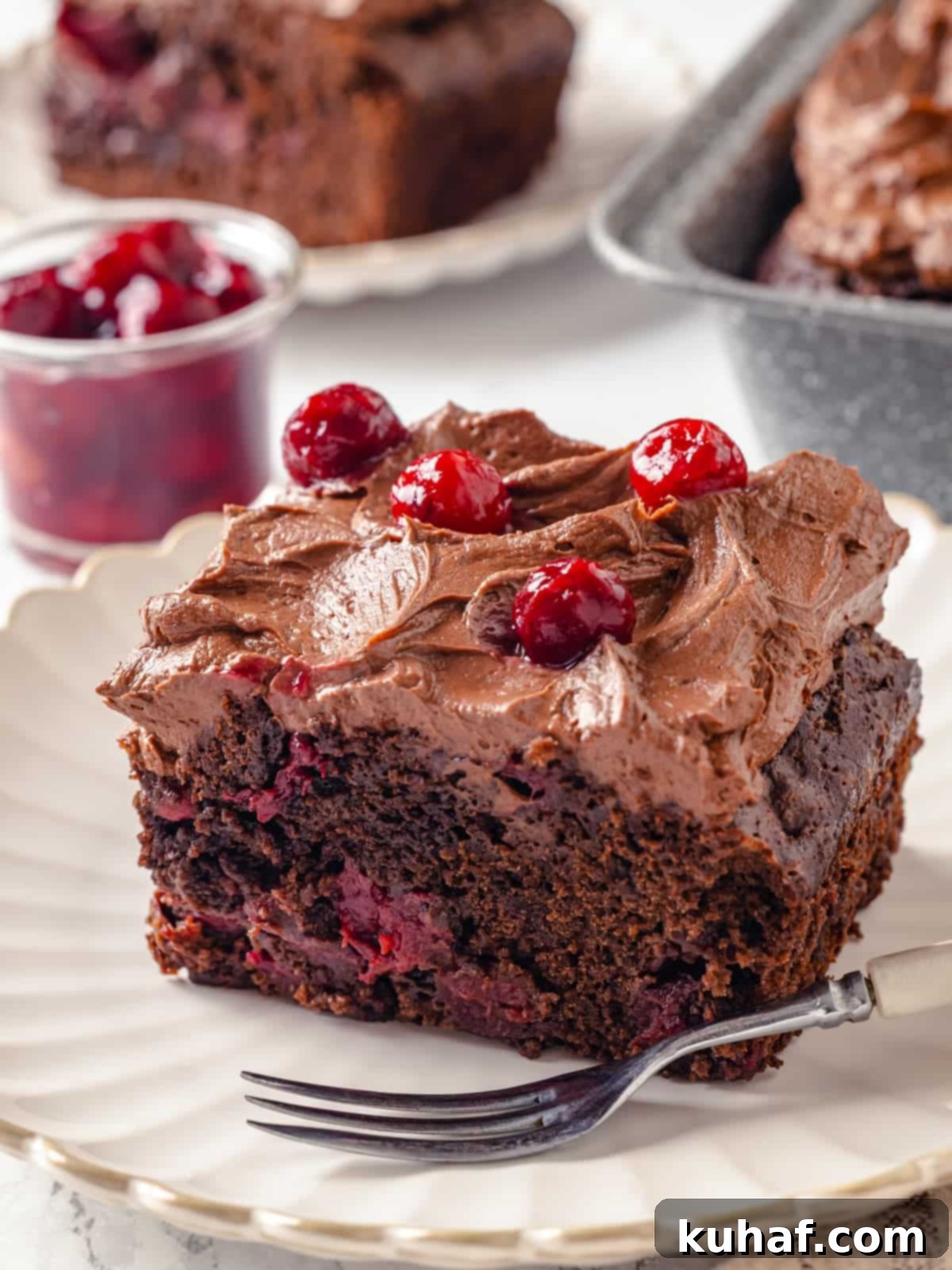 Slice of decadent chocolate cherry cake with textured frosting and cherry topping.