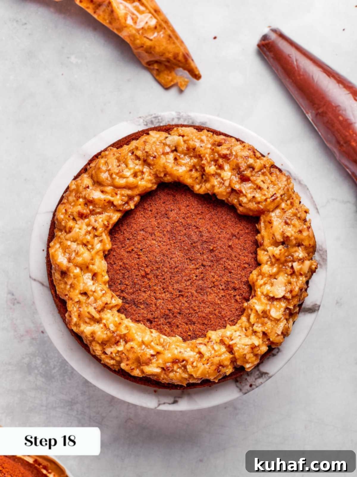 A ring of coconut pecan frosting piped around the edge of a cake layer, creating a dam to hold the ganache filling.
