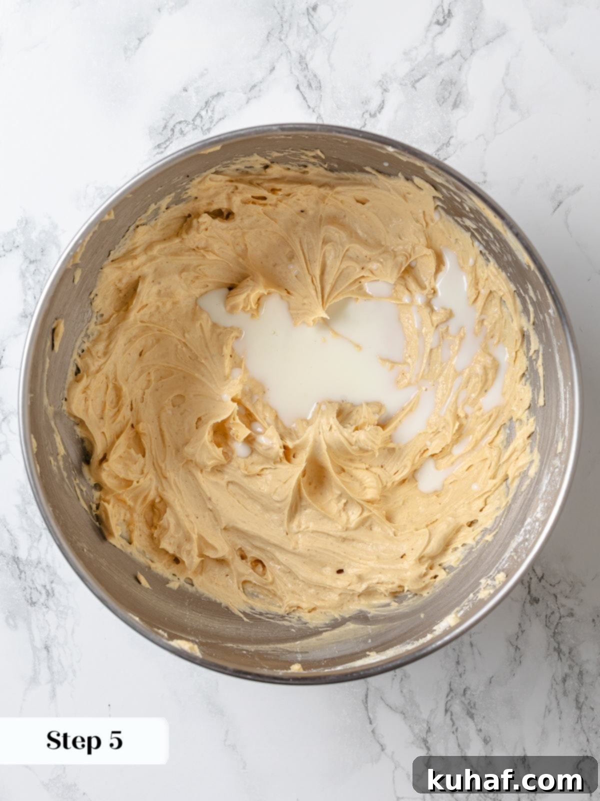 Cold heavy cream being poured into the frosting mixture before whipping the light peanut butter buttercream.