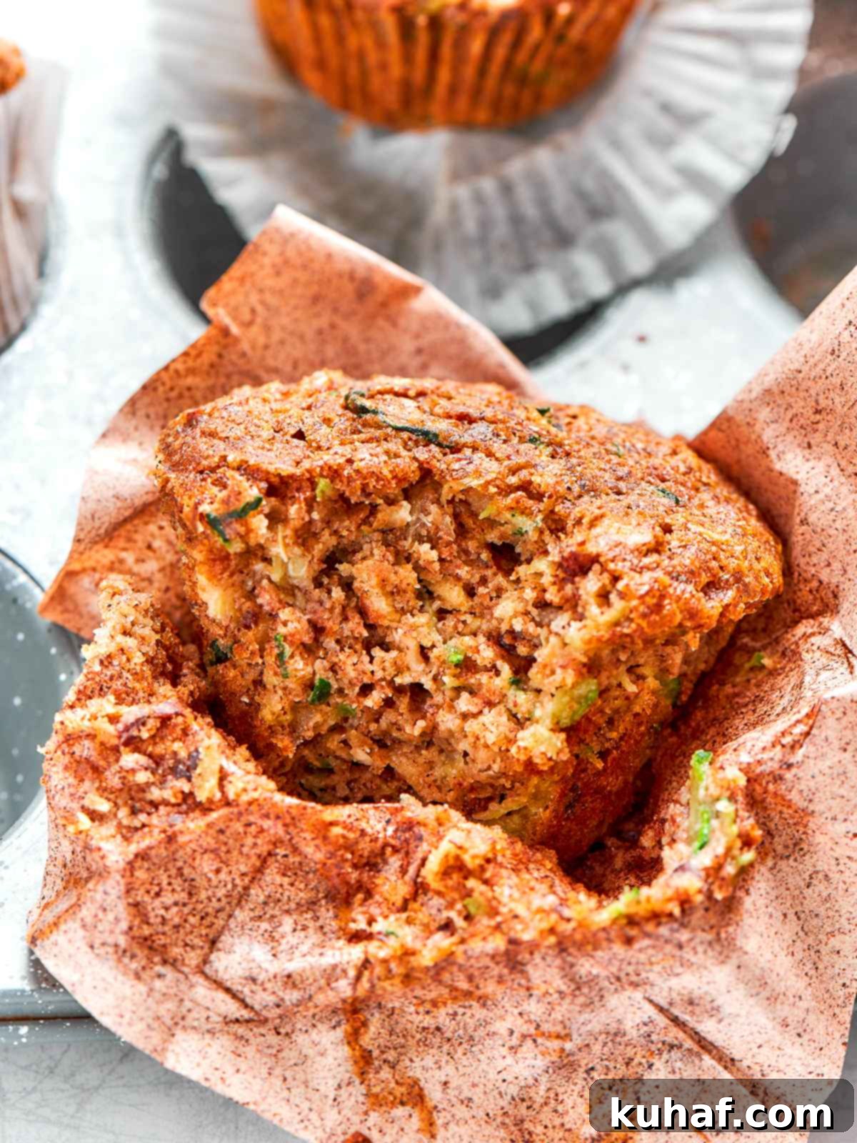 Zucchini muffin split open revealing soft tender crumb and flecks of zucchini.