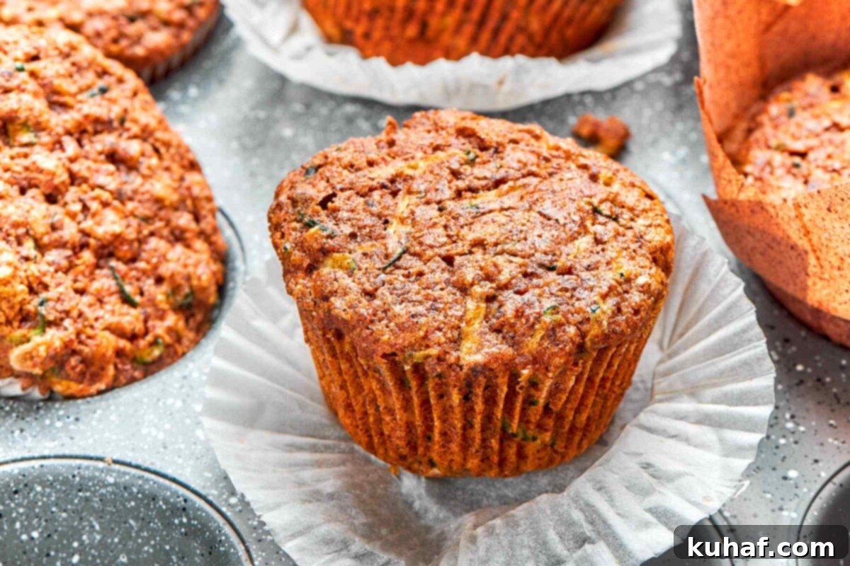 Zucchini muffin with wrapper peeled down revealing moist crumb and flecks of zucchini.